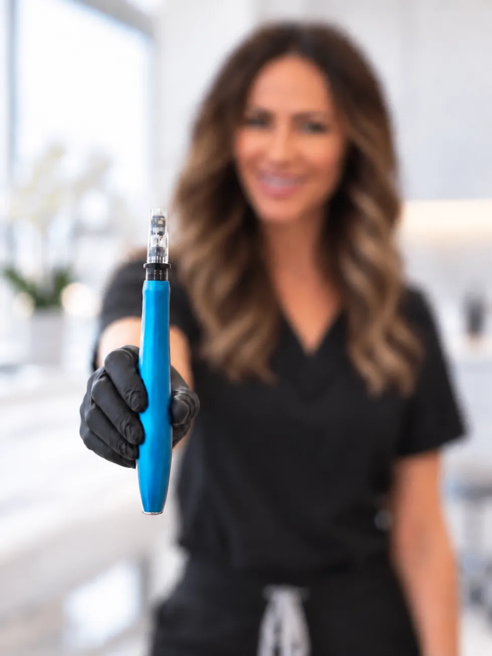 Practitioner in black presenting a microneedling device in a bright clinic